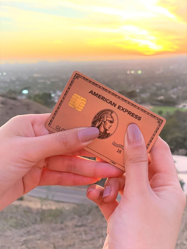 A person waving a gold American Express card in the air. The card has special benefits from itsagloriousworld.com  